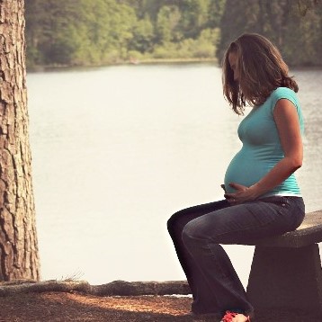 pregnant woman seated on a bench in a wooded park