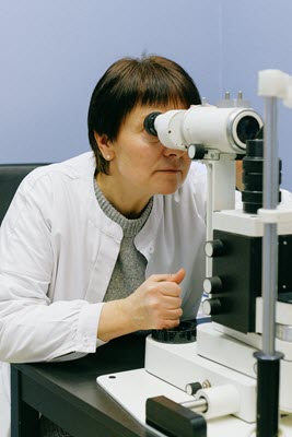 health care professional is examining a specimen with her microscope