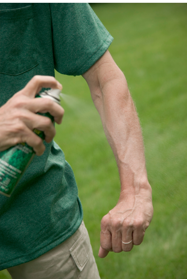 adult man spraying insect repellent on exposed skin on his arm